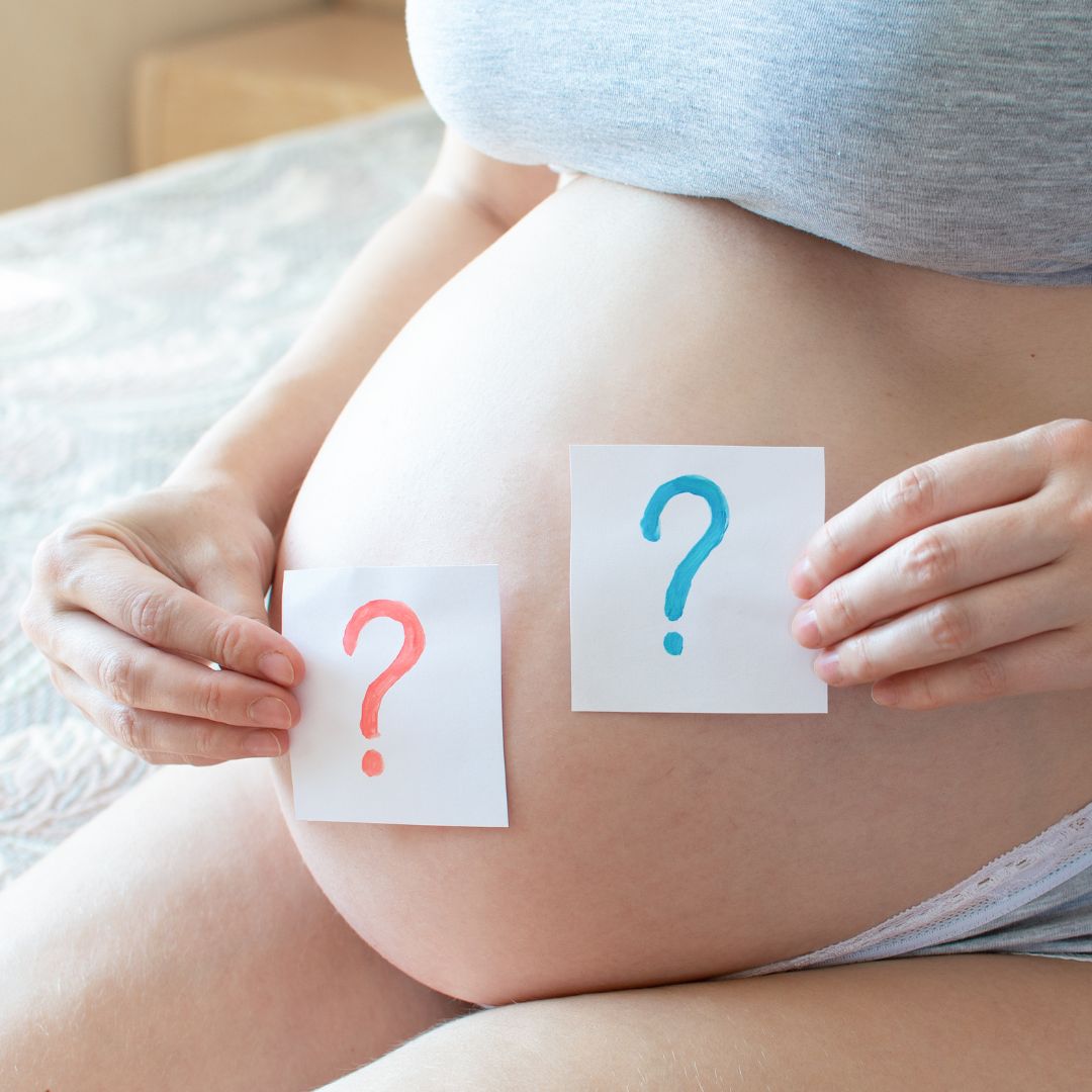 a woman holding a blue and pink question mark in front of her pregnant belly Sweet Baby Face services