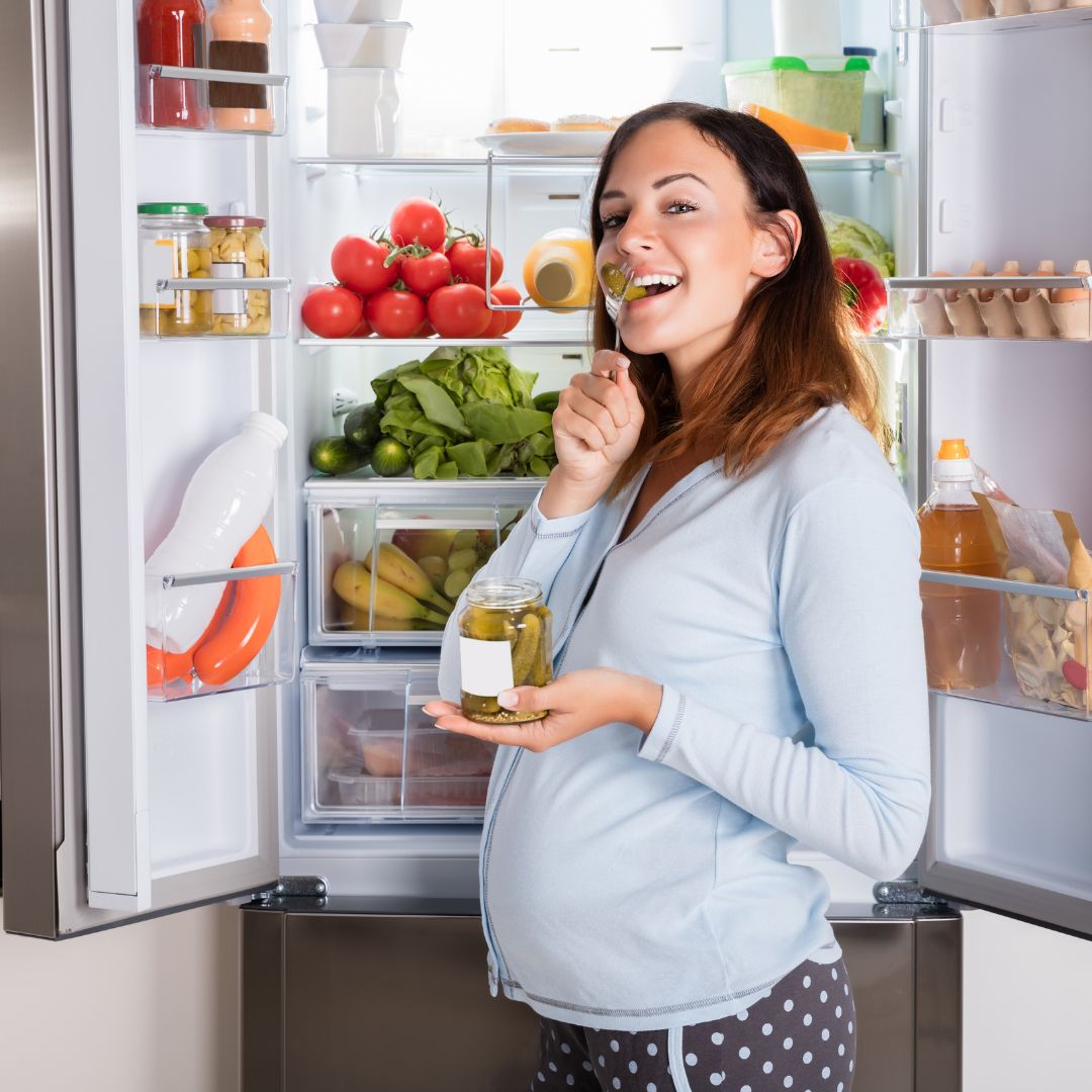 pregnant woman standing in front of a fridge filled with healthy foods